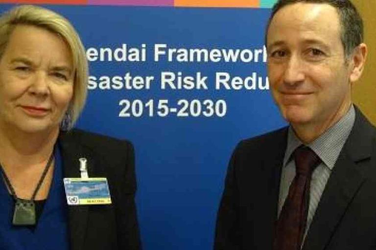Two people stand in front of a sign that reads "Sendai Framework Disaster Risk Reduction 2015-2030.