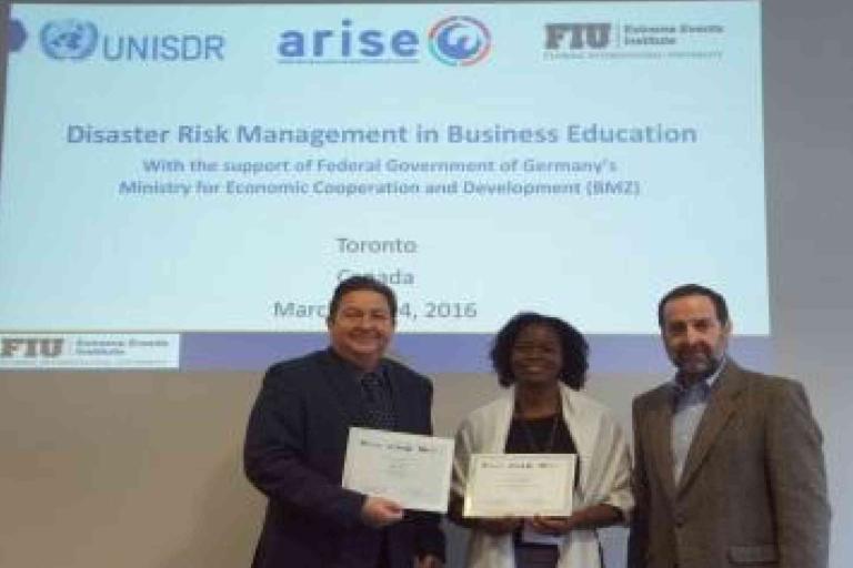 Three people stand in front of a screen displaying "Disaster Risk Management in Business Education" at an event in Toronto on March 24, 2016, holding certificates.