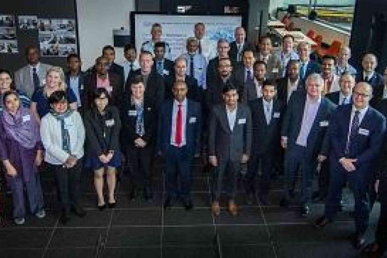 A diverse group of men and women in business attire stand together indoors, posing for a group photo at a professional event.