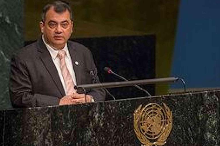 A man in a suit speaks at a podium with the United Nations emblem during a formal event or assembly.