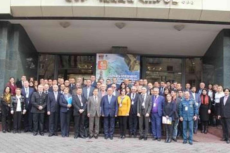 A large group of people in formal attire pose for a photo in front of a building entrance with a banner above the door.