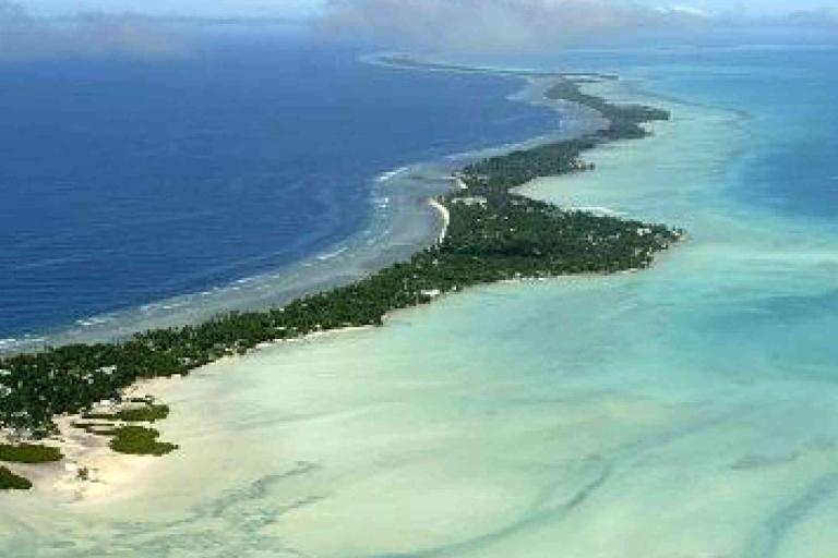 Aerial view of a narrow tropical island surrounded by turquoise shallows and deep blue ocean, with scattered vegetation and sandy beaches.