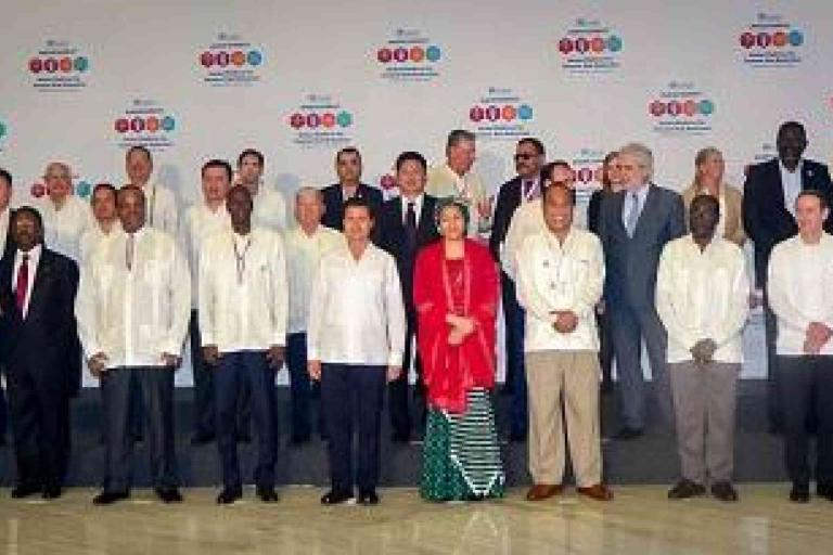 A group of delegates in formal attire pose for a photo in front of a conference backdrop with logos and event branding.