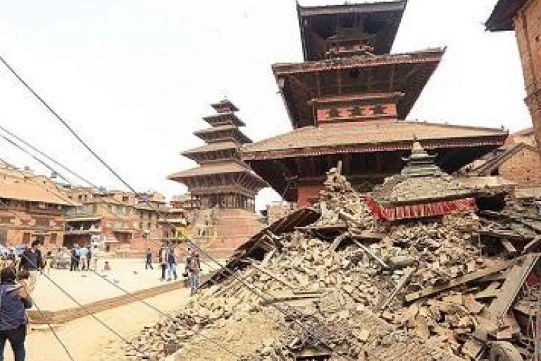 Collapsed historic temple with a large pile of debris in front, surrounded by other buildings and people observing the damage in a public square.