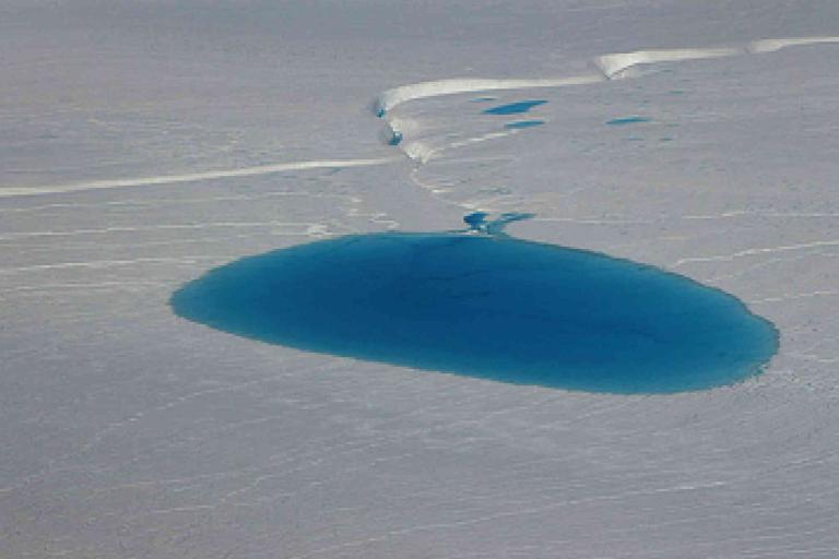 A large, deep blue meltwater pool sits on the surface of an ice sheet with cracks and smaller pools nearby.