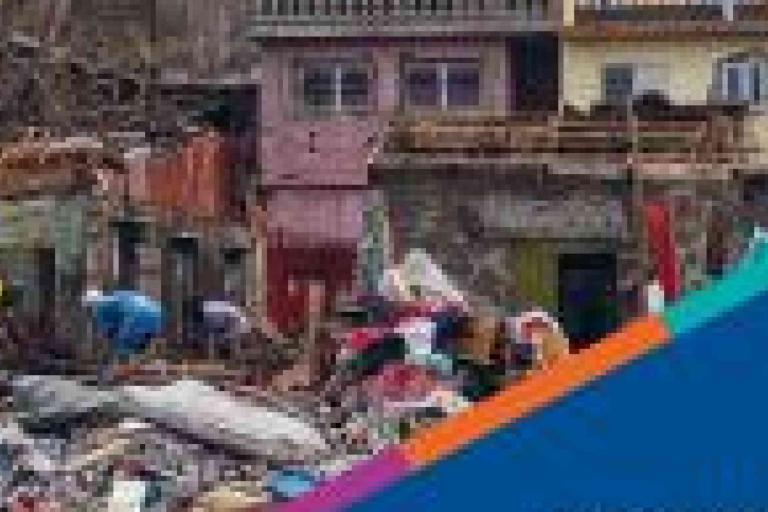 People search through debris in front of damaged buildings; piles of rubble and destroyed materials are visible.
