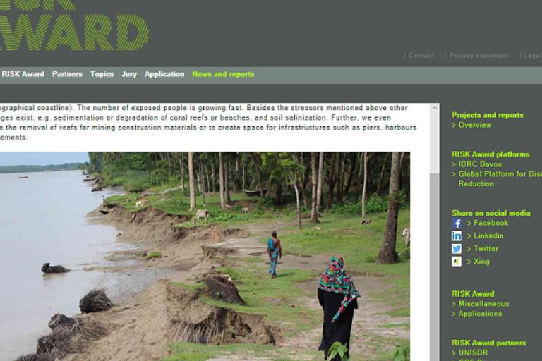Eroded riverbank with trees and exposed roots; two people walk along the edge, one in colorful clothing, under a cloudy sky.