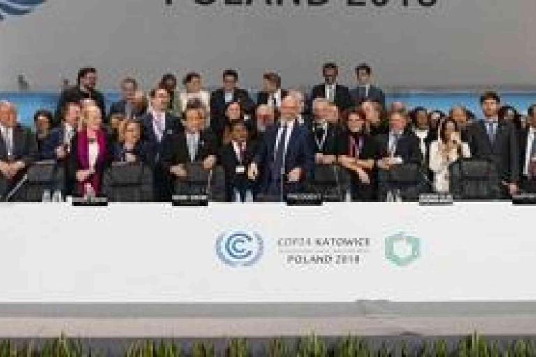 A large group of people in formal attire stands on a stage behind a table at the COP24 climate conference in Poland, 2018.