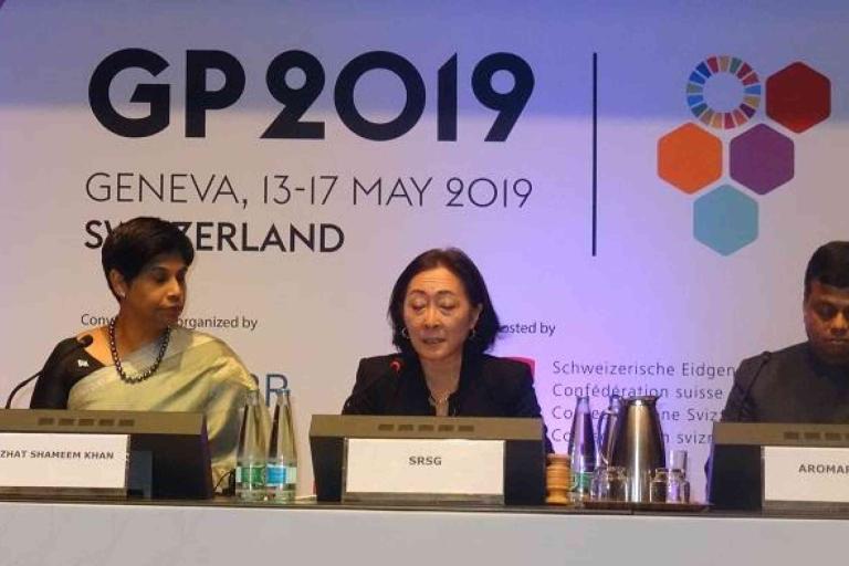 Three panelists sit at a table during the GP2019 conference in Geneva, Switzerland, with nameplates and microphones in front of them.