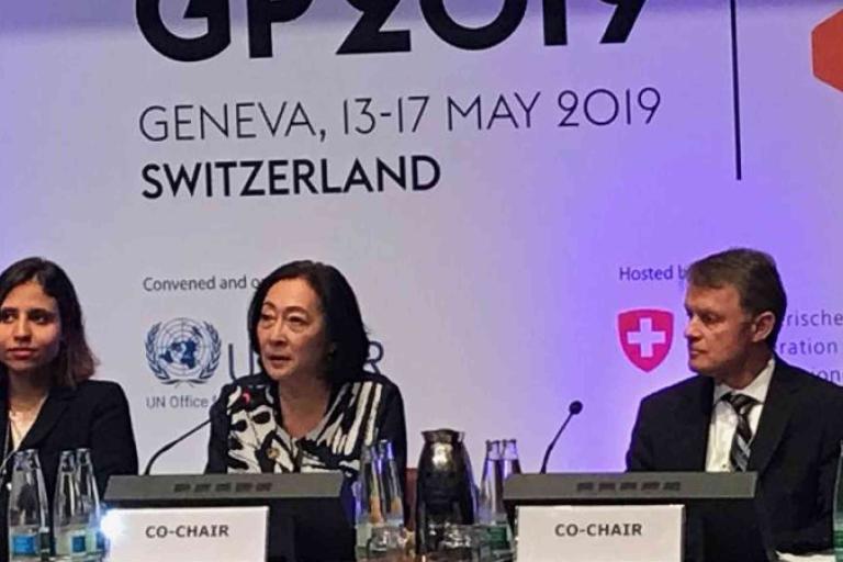 Three panelists sit at a table with microphones during the GP 2019 event in Geneva, Switzerland, with event signage visible behind them.