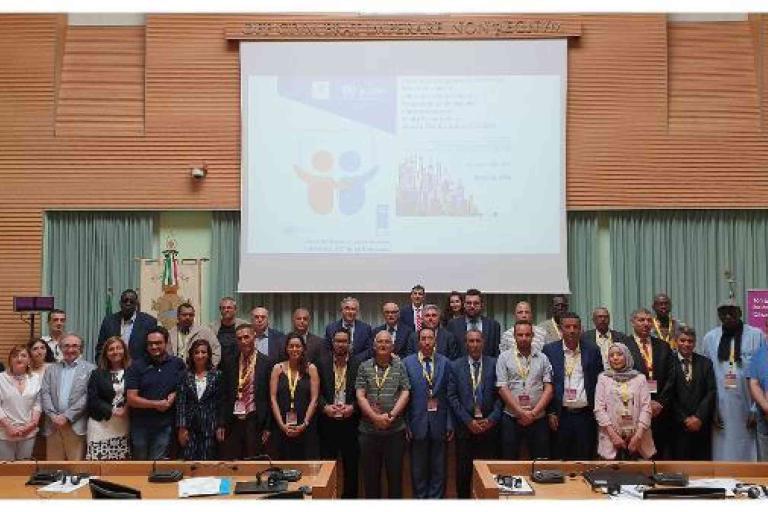A group of people in business attire pose for a group photo in a conference room, with a presentation projected on a screen behind them.