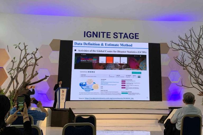 A speaker presents a slide on data definition and estimate methods at the IGNITE STAGE in a conference room, with attendees seated and some taking photos.