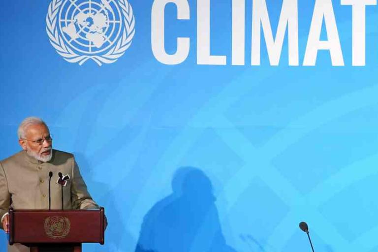 A man speaks at a podium in front of a blue backdrop displaying the United Nations emblem and the word "CLIMATE.