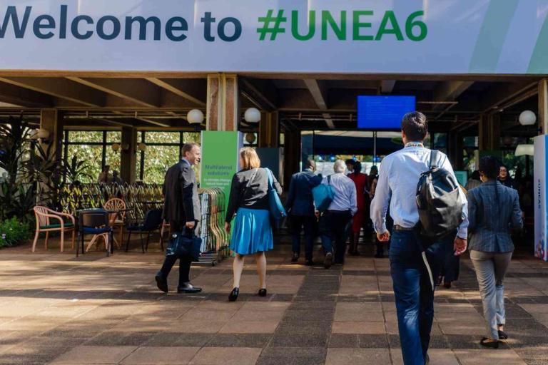 People walk toward an entrance under a “Welcome to #UNEA6” sign at what appears to be a conference or event venue.