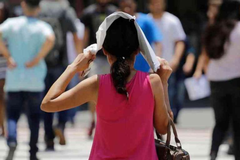A woman covers her head with a cloth while walking outdoors among a crowd of people.