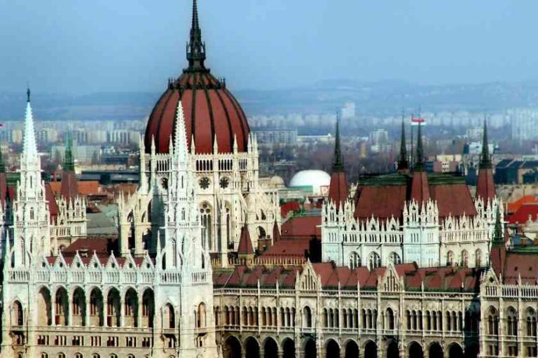 Hungarian Parliament Building with its central dome and spires, set against a cityscape background under a clear sky.