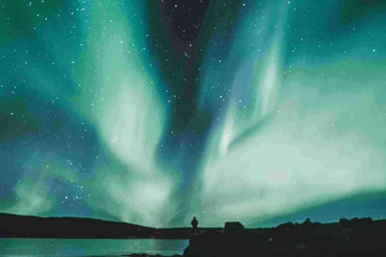 The aurora borealis displays streaks of green and blue light across a starry night sky above a silhouetted landscape.