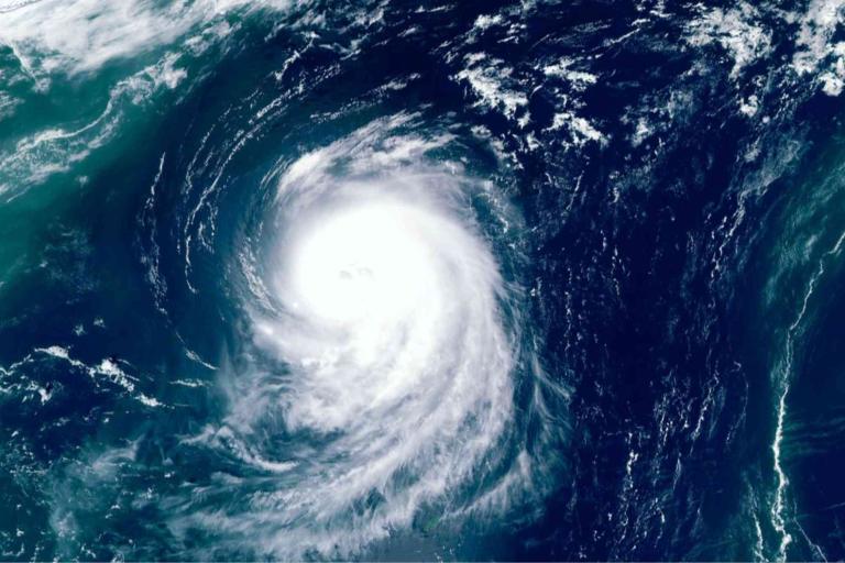 Satellite image shows a large hurricane swirling over the ocean, with a well-defined eye at the center and spiral cloud bands extending outward.