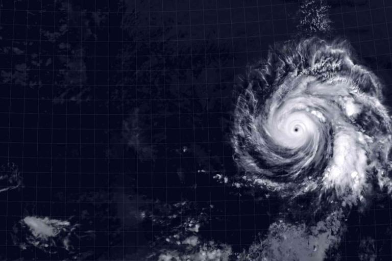 Satellite image shows a large hurricane with a well-defined eye swirling over the ocean, surrounded by cloud bands and clear grid lines marking coordinates.