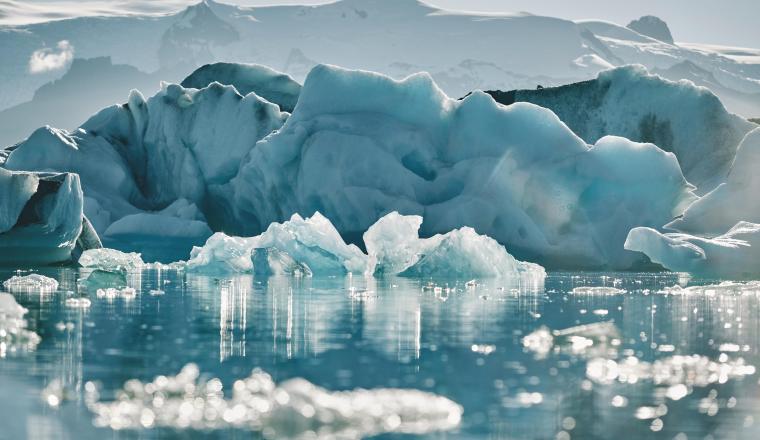 Glacial icebergs floating in a calm, icy water with a hazy mountain backdrop.