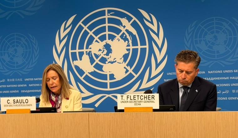 Celeste Saulo and Tom Fletcher sit at a table in front of a United Nations backdrop with nameplates identifying them.