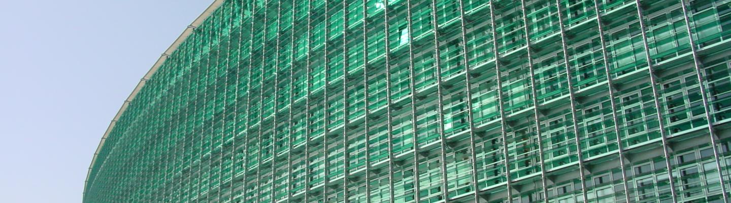 A large, modern glass building with a curved façade and green-tinted windows photographed from a low angle on a clear day.