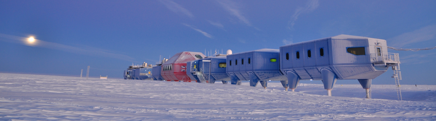 The Halley VI Research Station, a series of connected modular buildings on hydraulic legs, sits on an expanse of snow under a twilight sky.