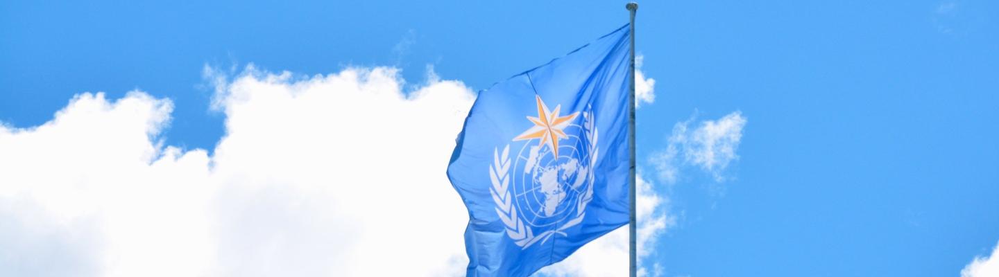The World Meteorological Organization flag flying against a blue sky with white clouds.