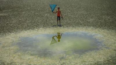 Child standing near a dry lake holding a kite