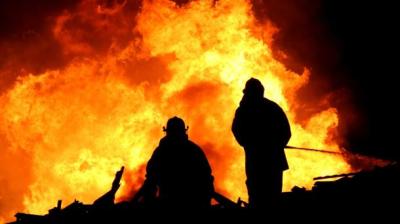 Two firefighters standing in front of a large fire.