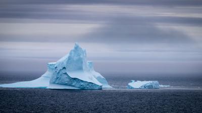Two icebergs floating in the ocean under a cloudy sky.