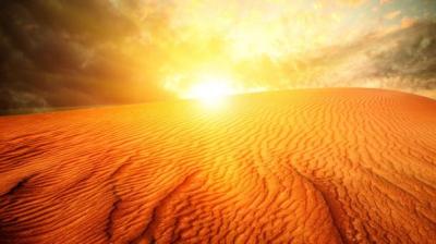 The sun rises over a sand dune in the desert.