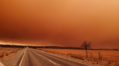 A car is driving down a road with a large orange dust storm in the distance.