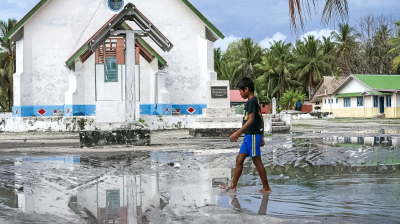 A boy walks through a puddle in front of a church.