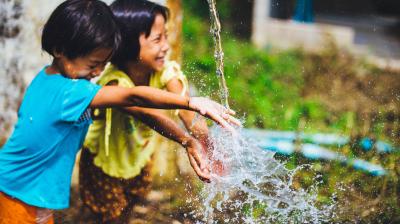 Two children playing with water from a water pipe.
