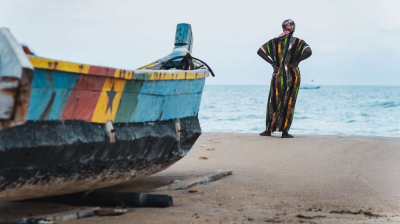 A man standing next to a colorful boat on the beach.