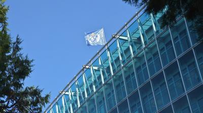 The flag of the united nations flies over a glass building.