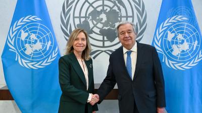 Two people shaking hands in front of un flags.