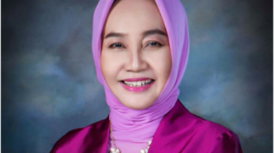A woman wearing a purple hijab smiles for the camera.