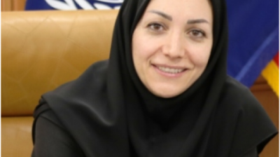 A woman in a black hijab smiling in front of flags.