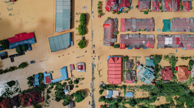 Aerial view of a flooded urban area with submerged streets and partially covered rooftops of colorful houses.