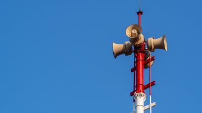 Four loudspeakers mounted on a red and white pole against a clear blue sky.