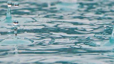 Raindrops hitting the surface of a body of water, creating ripples and small splashes.