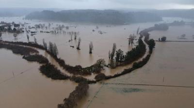 An aerial view of extensive flooding in a rural area of Chile, where fields are submerged under muddy water, and trees and structures are partially inundated.