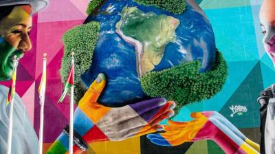 Colorful mural depicting a man and a child holding up a globe together, surrounded by vibrant geometric patterns.