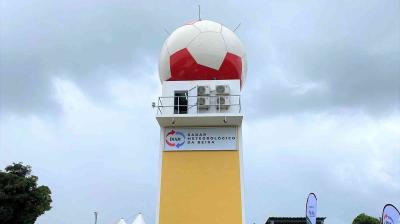 A tall structure with a large radar dome painted to resemble a red and white soccer ball is labeled "Radar Meteorológico da Beira" against a cloudy sky.