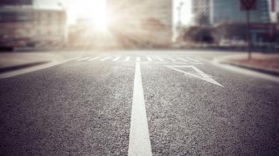 Empty city street intersection at sunrise with visible road markings, including a straight arrow and a pedestrian crosswalk.