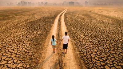 Two people stand on a dry, cracked path leading toward a distant city skyline under a hazy sky.