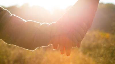 Two people holding hands with a bright sunlit background.