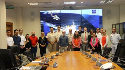 Group of people posing in a conference room with a large screen displaying a ship at sea in the background.